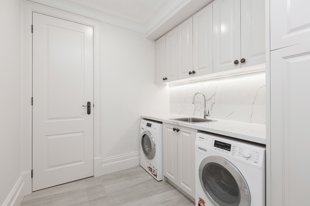 Idéer för att renovera en stor vintage linjär tvättstuga enbart för tvätt, med en undermonterad diskho, vita skåp, marmorbänkskiva, vita väggar, marmorgolv, en tvättmaskin och torktumlare bredvid varandra och grått golv