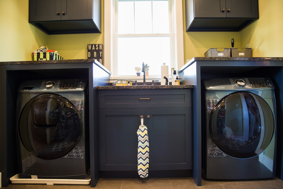 Idee per una lavanderia multiuso tradizionale di medie dimensioni con lavello a doppia vasca, ante con riquadro incassato, ante blu, top in granito, pareti gialle, pavimento con piastrelle in ceramica, lavatrice e asciugatrice affiancate, pavimento beige e top nero