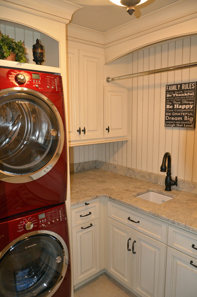 Ejemplo de lavadero multiusos clásico con fregadero bajoencimera, puertas de armario blancas, encimera de granito, lavadora y secadora apiladas y armarios con paneles con relieve