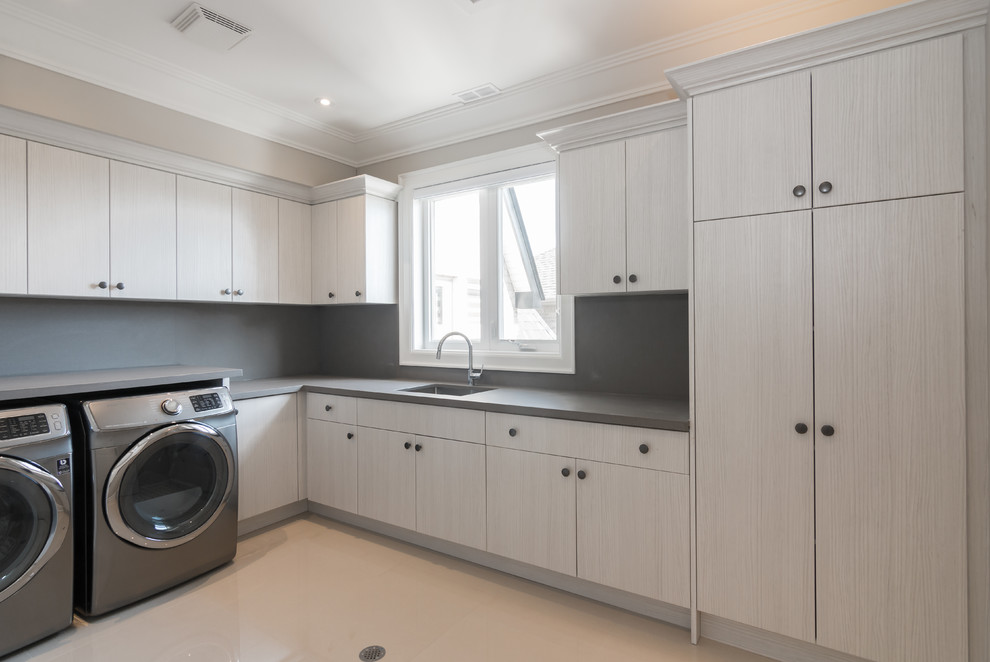 This is an example of a large contemporary l-shaped separated utility room in Toronto with a submerged sink, flat-panel cabinets, grey cabinets, concrete worktops, beige walls, concrete flooring, a side by side washer and dryer and beige floors.