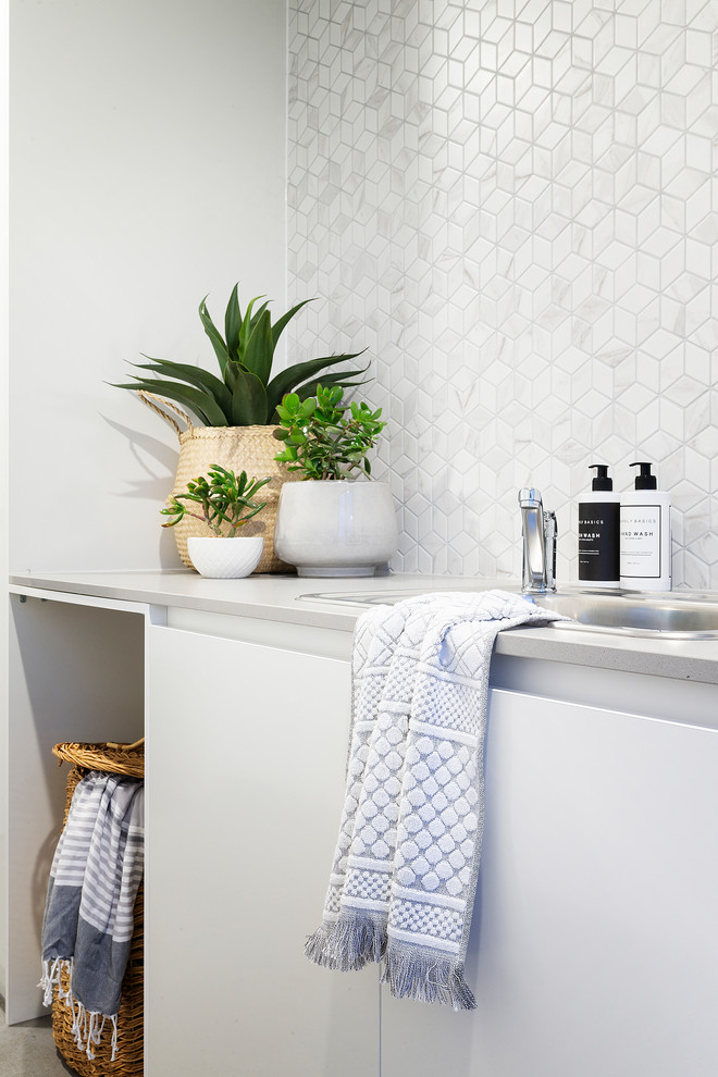 Foto på en mellanstor funkis grå linjär tvättstuga enbart för tvätt, med en nedsänkt diskho, vita skåp, bänkskiva i kvarts, vita väggar, klinkergolv i porslin, en tvättmaskin och torktumlare bredvid varandra och grått golv