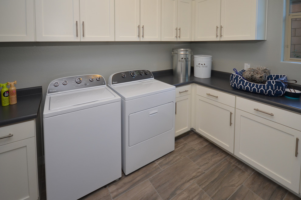 Dedicated laundry room - mid-sized modern l-shaped porcelain tile dedicated laundry room idea in Phoenix with recessed-panel cabinets, white cabinets, laminate countertops, gray walls and a side-by-side washer/dryer