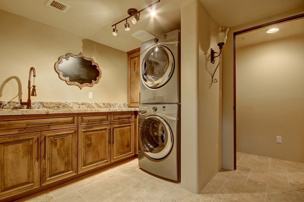 Inspiration for a mid-sized southwestern l-shaped travertine floor dedicated laundry room remodel in Phoenix with an undermount sink, raised-panel cabinets, dark wood cabinets, granite countertops, beige walls and a stacked washer/dryer