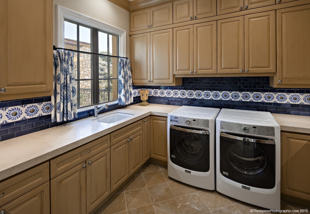 Klassisk inredning av en l-formad tvättstuga enbart för tvätt, med en undermonterad diskho, luckor med infälld panel, skåp i ljust trä, granitbänkskiva, marmorgolv och en tvättmaskin och torktumlare bredvid varandra