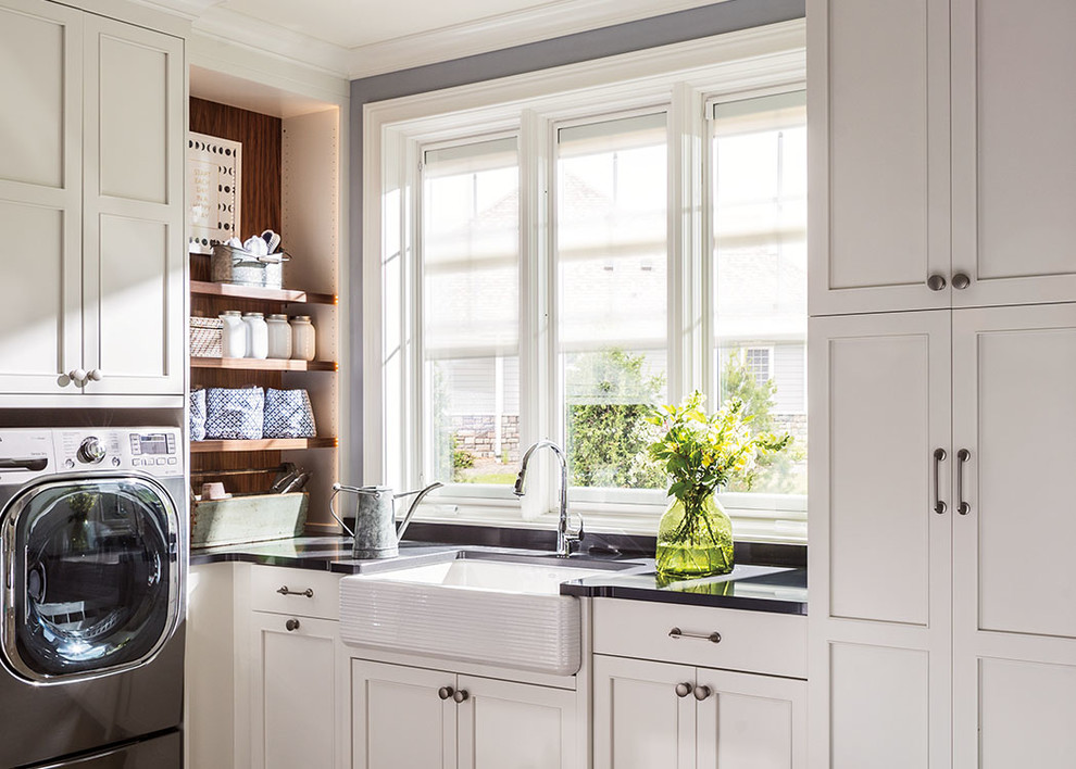 Photo of a traditional u-shaped separated utility room in Indianapolis with a belfast sink, shaker cabinets, white cabinets, grey walls, a side by side washer and dryer and black worktops.