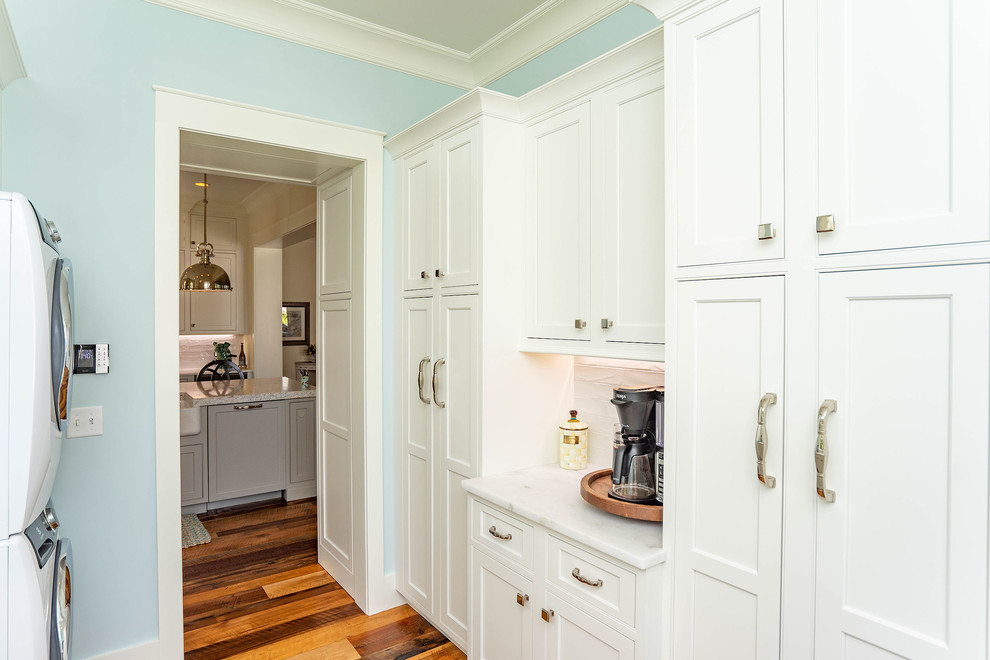 This is an example of a medium sized beach style galley utility room in Atlanta with shaker cabinets, white cabinets, quartz worktops, blue walls, dark hardwood flooring, a stacked washer and dryer, brown floors and white worktops.