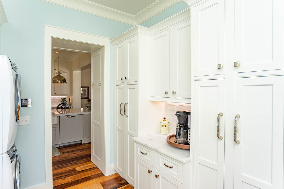 Foto de lavadero multiusos y de galera costero de tamaño medio con armarios estilo shaker, puertas de armario blancas, encimera de cuarcita, paredes azules, suelo de madera oscura, lavadora y secadora apiladas, suelo marrón y encimeras blancas