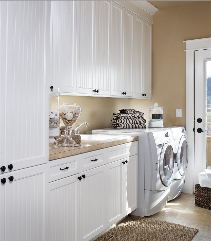 Bild på en mellanstor lantlig linjär tvättstuga enbart för tvätt, med en nedsänkt diskho, släta luckor, vita skåp, laminatbänkskiva, beige väggar, klinkergolv i porslin och en tvättmaskin och torktumlare bredvid varandra