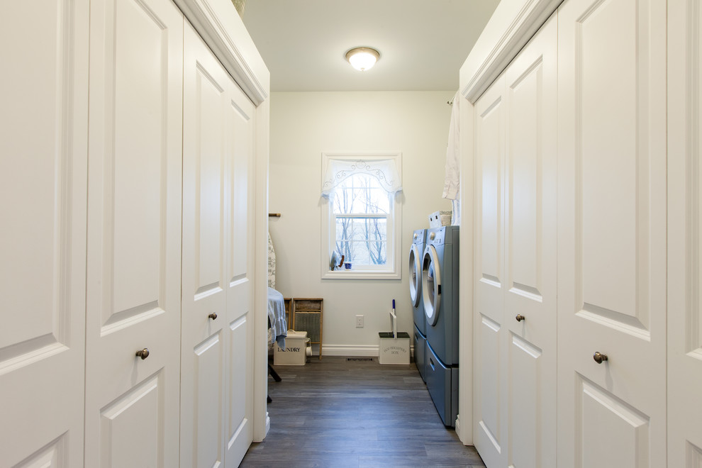 Foto di una sala lavanderia stile shabby di medie dimensioni con ante con bugna sagomata, ante bianche, pareti bianche, lavatrice e asciugatrice affiancate, pavimento in legno massello medio e pavimento marrone