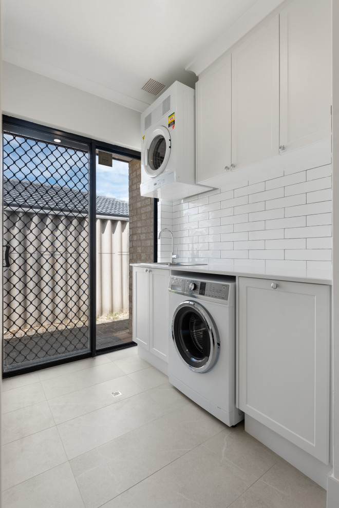 Inspiration for a mid-sized modern single-wall ceramic tile and white floor dedicated laundry room remodel in Perth with a drop-in sink, recessed-panel cabinets, white cabinets, white walls and white countertops