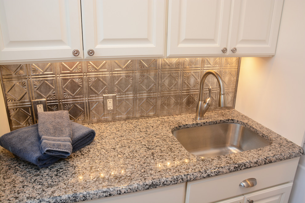 Inspiration för små klassiska linjära grått tvättstugor enbart för tvätt, med en undermonterad diskho, luckor med upphöjd panel, vita skåp, granitbänkskiva, stänkskydd med metallisk yta, grå väggar och en tvättpelare