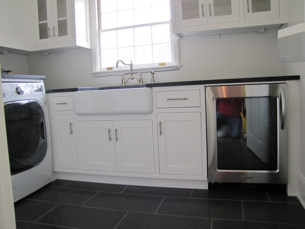 Bild på ett amerikanskt parallellt grovkök, med en rustik diskho, vita skåp, bänkskiva i täljsten, vita väggar, klinkergolv i porslin, en tvättmaskin och torktumlare bredvid varandra och skåp i shakerstil