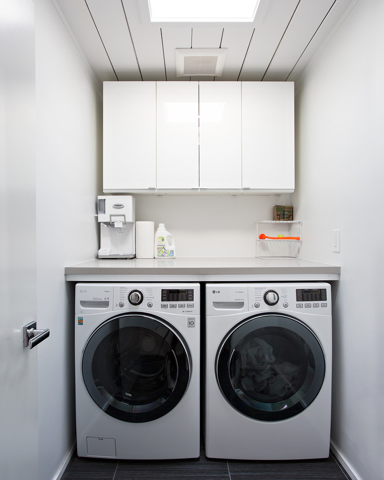 This is an example of a small midcentury single-wall separated utility room in San Francisco with flat-panel cabinets, white cabinets, white walls, a side by side washer and dryer, black floors and grey worktops.