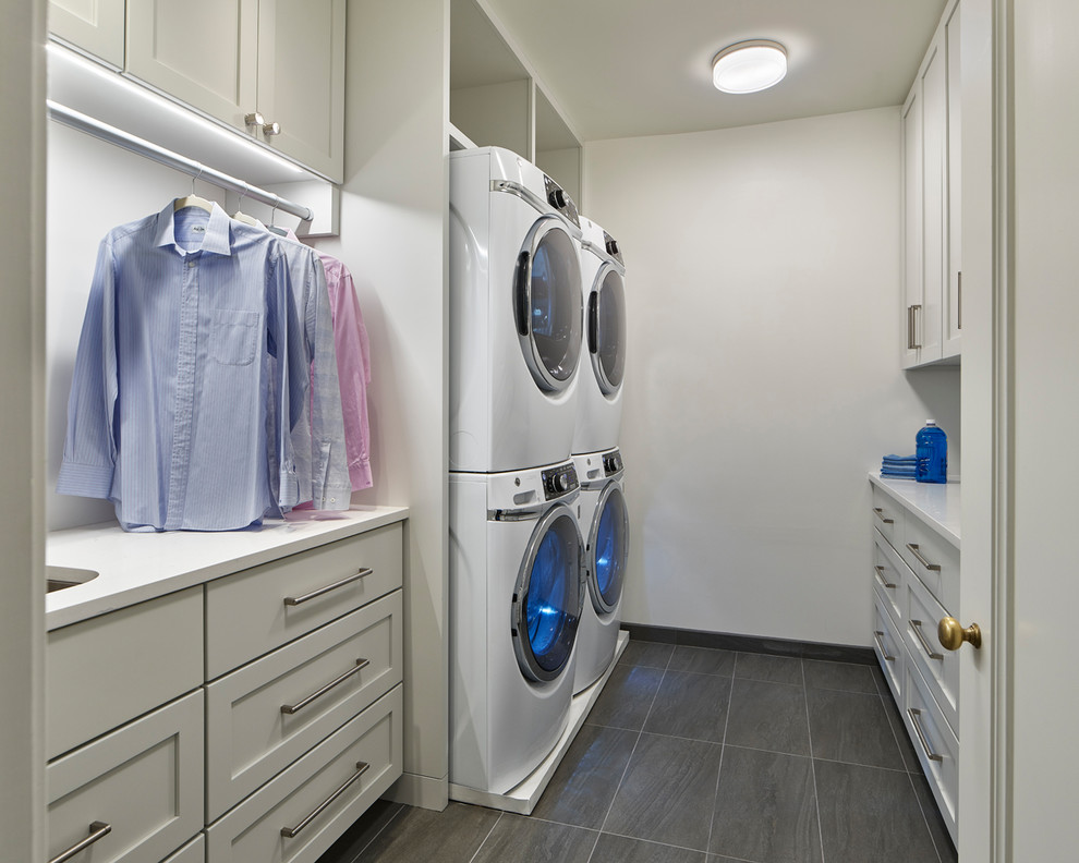 This is an example of a large traditional galley separated utility room in Philadelphia with a submerged sink, shaker cabinets, white cabinets, composite countertops, white walls, ceramic flooring, a stacked washer and dryer, grey floors and white worktops.