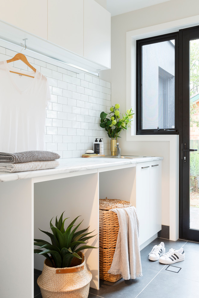 Inspiration för mellanstora moderna linjära vitt tvättstugor enbart för tvätt, med en enkel diskho, vita skåp, laminatbänkskiva, vita väggar, klinkergolv i porslin, en tvättmaskin och torktumlare bredvid varandra och grått golv