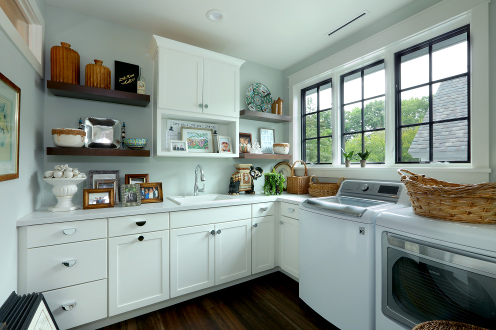 Bild på en stor lantlig vita l-formad vitt tvättstuga enbart för tvätt, med en enkel diskho, luckor med infälld panel, vita skåp, bänkskiva i kvartsit, grå väggar, mörkt trägolv och en tvättmaskin och torktumlare bredvid varandra
