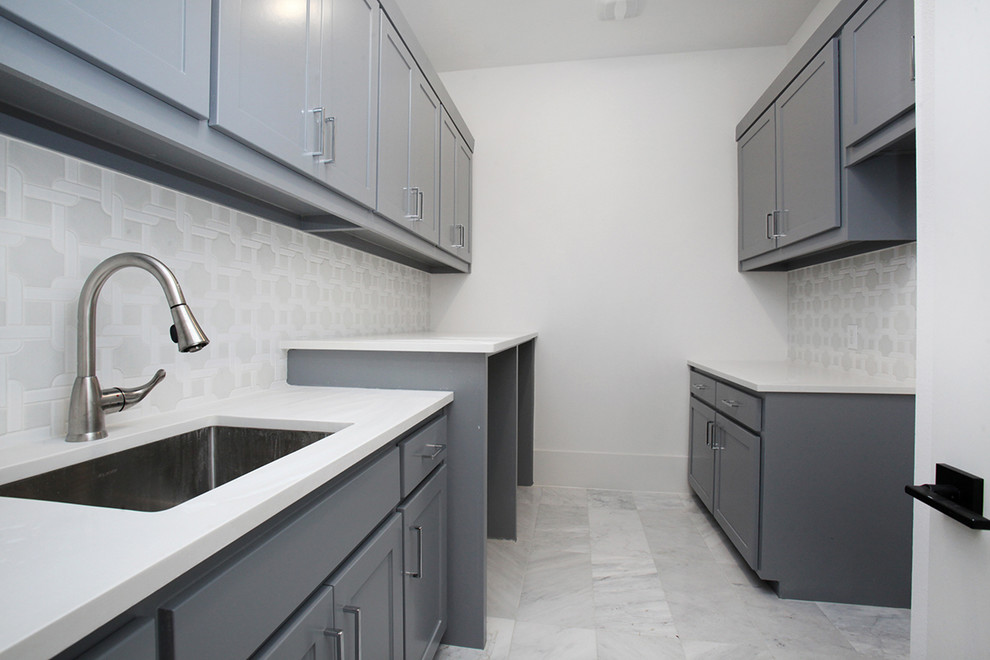This is an example of a large traditional galley utility room in Dallas with a submerged sink, shaker cabinets, grey cabinets, engineered stone countertops, white walls, marble flooring, an integrated washer and dryer, white floors and white worktops.