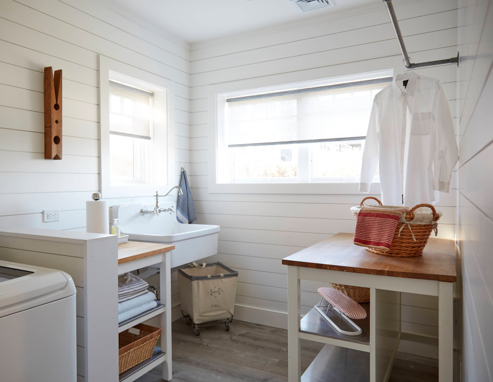 Large beach style laminate floor, gray floor and shiplap wall dedicated laundry room photo in Providence with a farmhouse sink, open cabinets, white cabinets, wood countertops, white walls and a side-by-side washer/dryer