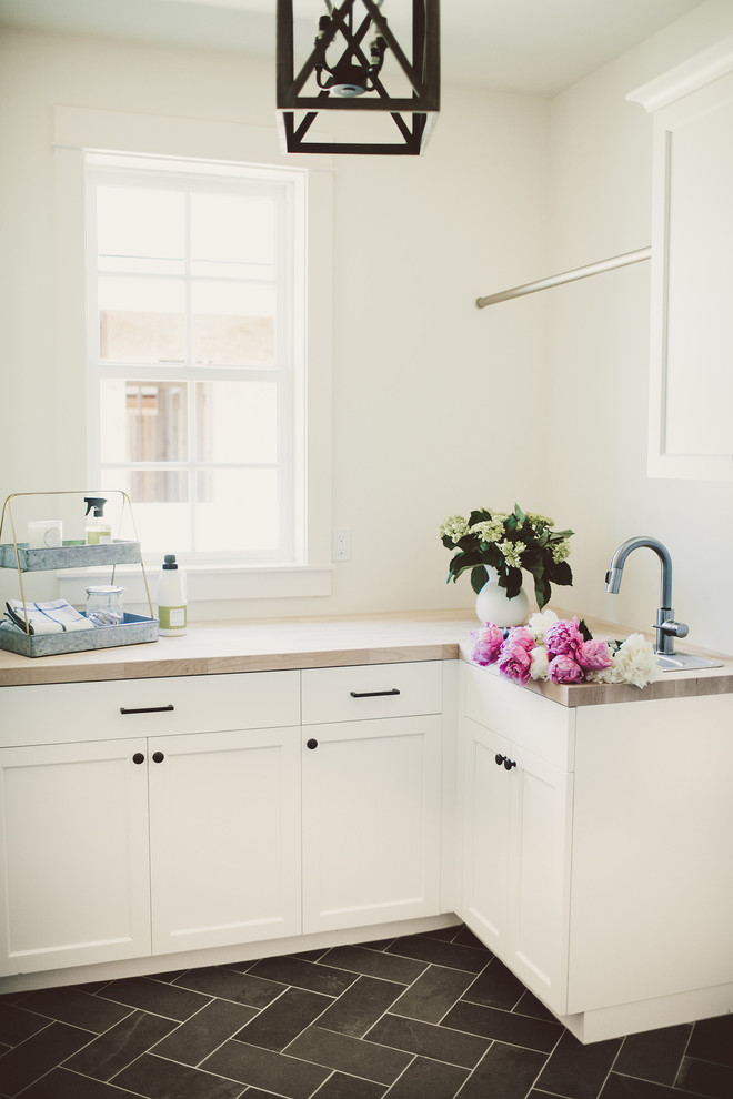 Dedicated laundry room - small farmhouse l-shaped slate floor dedicated laundry room idea in Portland with shaker cabinets, white cabinets, wood countertops, white walls, a side-by-side washer/dryer and a drop-in sink