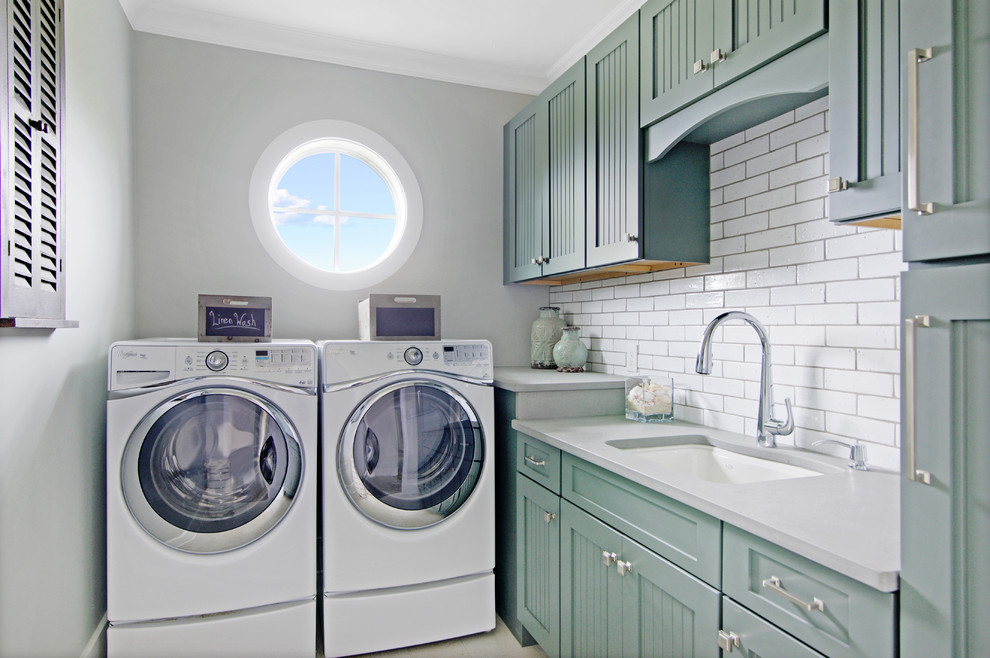 Foto di una piccola sala lavanderia costiera con lavello sottopiano, ante con riquadro incassato, lavatrice e asciugatrice affiancate, top grigio e ante blu
