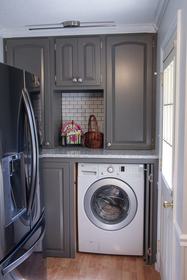 Foto på ett linjärt grovkök, med luckor med upphöjd panel, grå skåp, bänkskiva i kvartsit, grå väggar, mellanmörkt trägolv och tvättmaskin och torktumlare byggt in i ett skåp