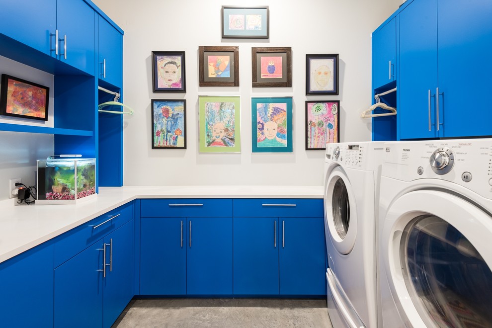 Imagen de cuarto de lavado en U actual con armarios con paneles lisos, puertas de armario azules, paredes blancas, lavadora y secadora juntas y encimeras blancas