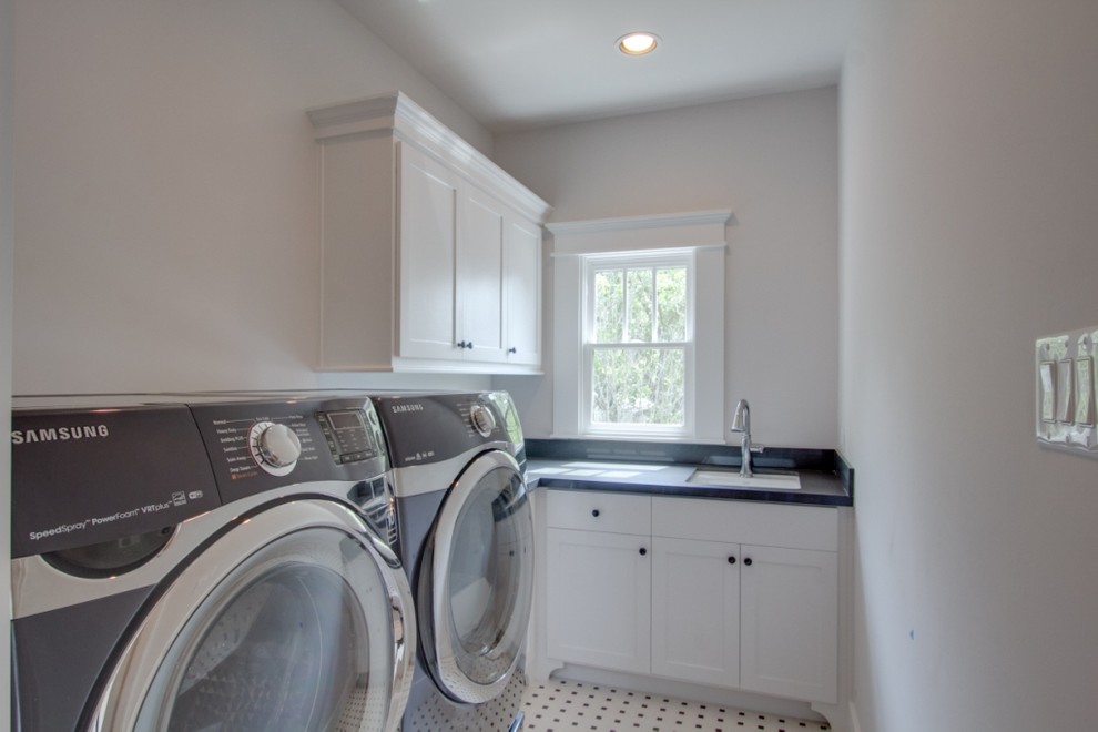 ヒューストンにある中くらいなトラディショナルスタイルのおしゃれな洗濯室 (シングルシンク、白いキャビネット、白い壁、セラミックタイルの床、左右配置の洗濯機・乾燥機、マルチカラーの床、青いキッチンカウンター) の写真