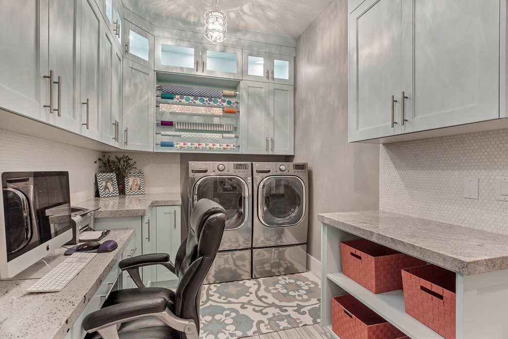 Klassisk inredning av ett stort l-format grovkök, med granitbänkskiva, grå väggar, klinkergolv i porslin, en tvättmaskin och torktumlare bredvid varandra, vitt golv, blå skåp och luckor med infälld panel