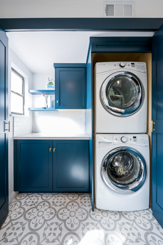 Ejemplo de cuarto de lavado lineal actual pequeño con armarios estilo shaker, puertas de armario azules, encimera de cuarcita, paredes blancas, suelo de baldosas de cerámica, lavadora y secadora apiladas y suelo blanco