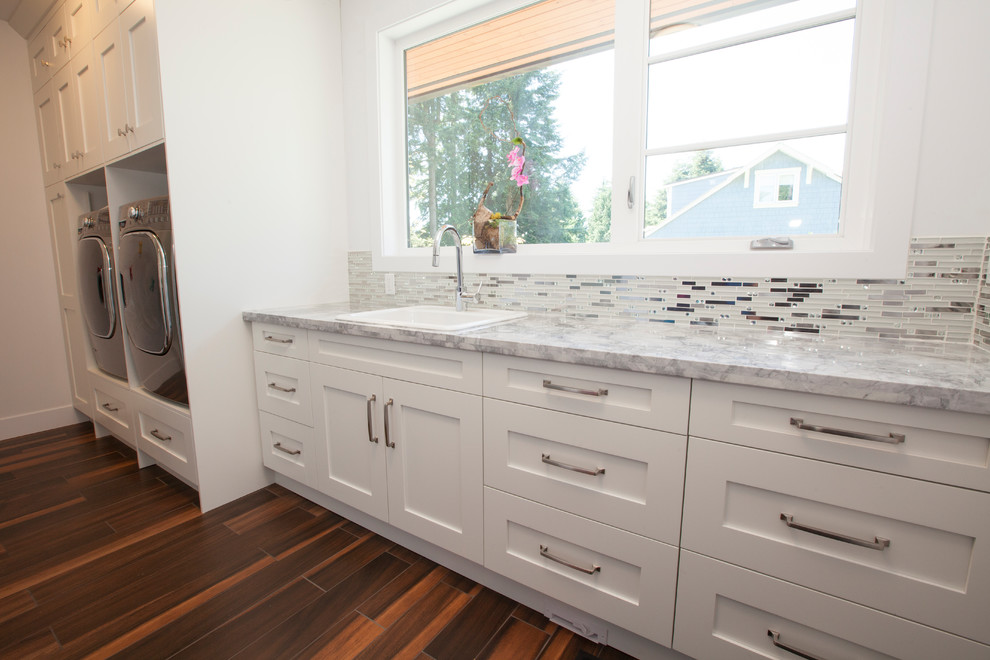 Einzeilige, Mittelgroße Moderne Waschküche mit Einbauwaschbecken, Schrankfronten im Shaker-Stil, weißen Schränken, Quarzwerkstein-Arbeitsplatte, weißer Wandfarbe, braunem Holzboden, Waschmaschine und Trockner nebeneinander und braunem Boden in Vancouver