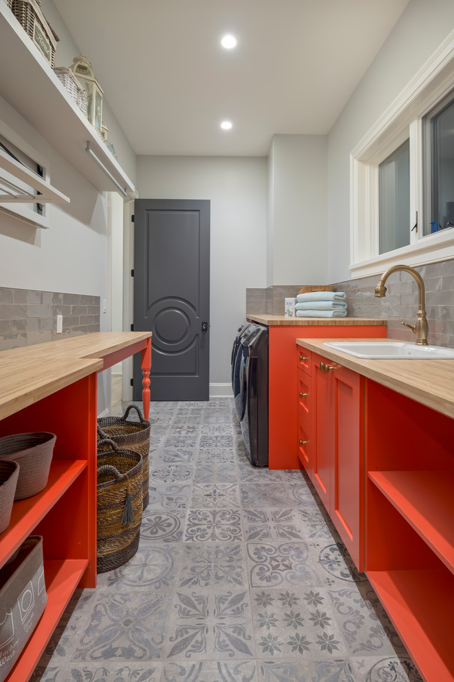Zweizeilige Maritime Waschküche mit Einbauwaschbecken, Schrankfronten im Shaker-Stil, orangefarbenen Schränken, Arbeitsplatte aus Holz, grauer Wandfarbe, Waschmaschine und Trockner nebeneinander, grauem Boden und beiger Arbeitsplatte in Vancouver