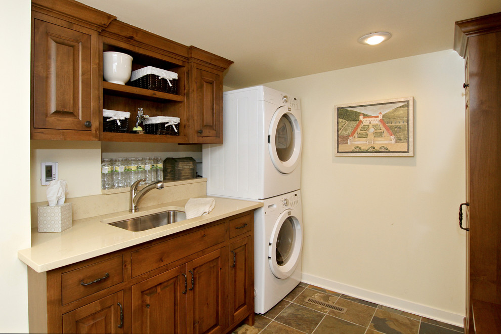 Uriger Hauswirtschaftsraum mit hellbraunen Holzschränken, beiger Wandfarbe und Waschmaschine und Trockner gestapelt in Minneapolis