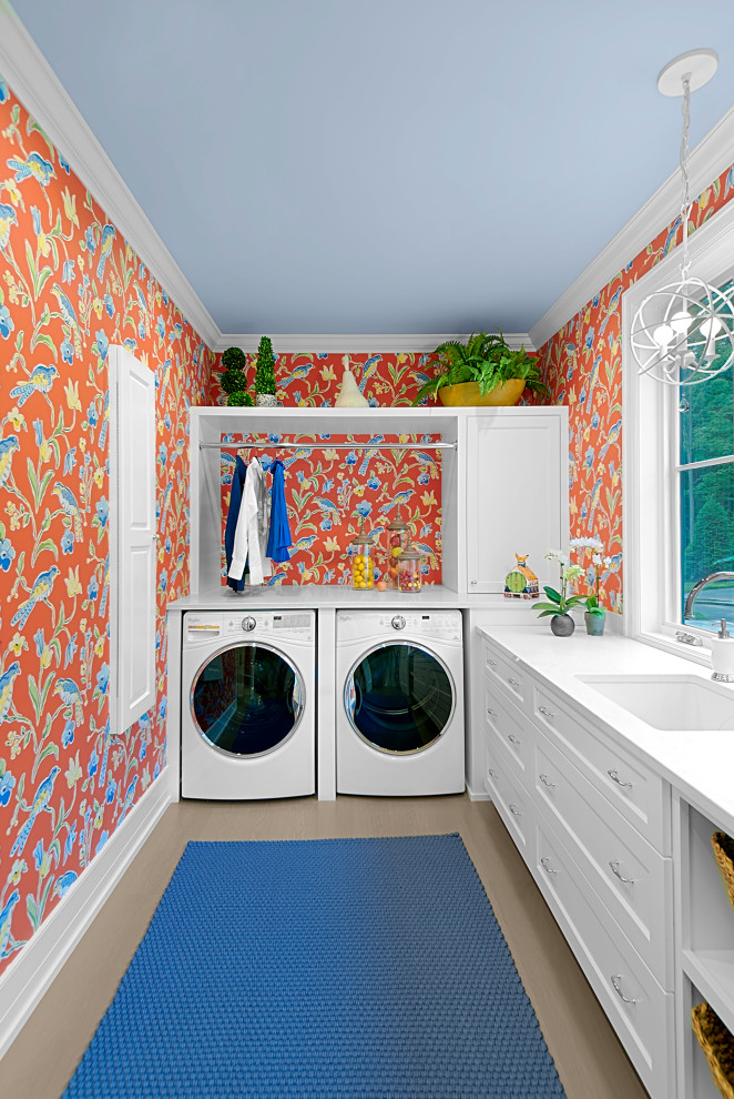 Inspiration for a large traditional l-shaped utility room in Grand Rapids with a submerged sink, shaker cabinets, white cabinets, multi-coloured walls, a side by side washer and dryer, white worktops, wallpapered walls, engineered stone countertops, window splashback, medium hardwood flooring and brown floors.