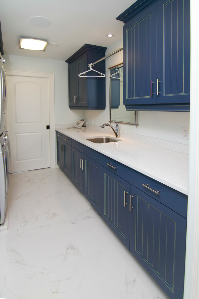 Zweizeilige, Mittelgroße Klassische Waschküche mit Unterbauwaschbecken, flächenbündigen Schrankfronten, blauen Schränken, Mineralwerkstoff-Arbeitsplatte, weißer Wandfarbe, Marmorboden und Waschmaschine und Trockner gestapelt in Toronto