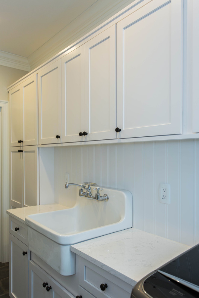 Example of a mid-sized transitional single-wall concrete floor and gray floor dedicated laundry room design in Boston with recessed-panel cabinets, white cabinets, quartz countertops, a side-by-side washer/dryer, a farmhouse sink and beige walls