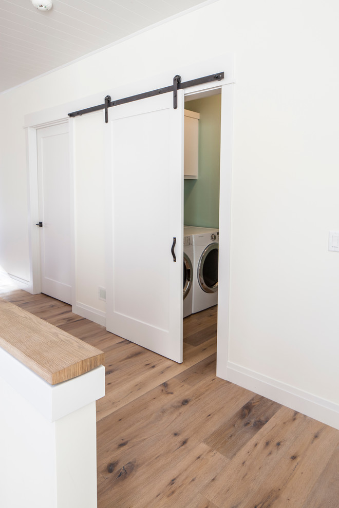 Foto di un ripostiglio-lavanderia minimalista di medie dimensioni con ante in stile shaker, ante bianche, pareti verdi, parquet chiaro e lavatrice e asciugatrice affiancate