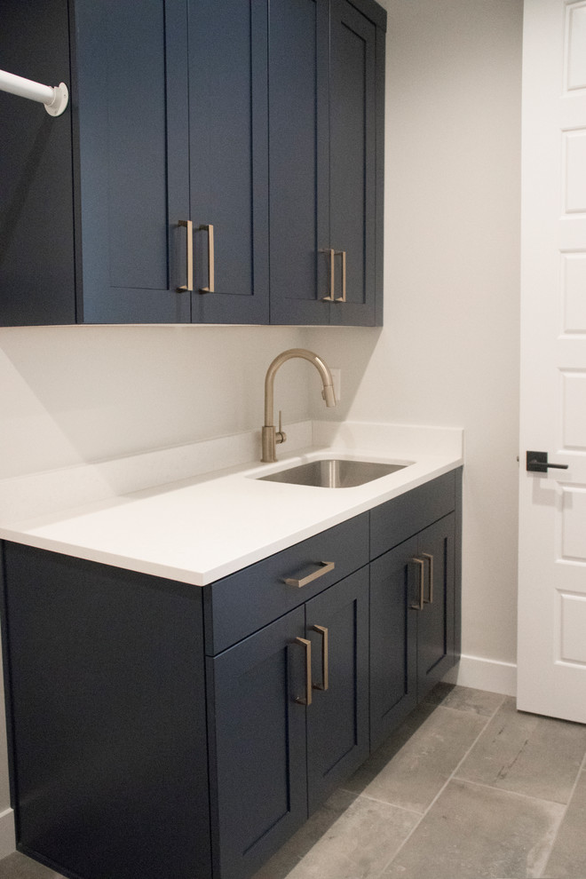 Mid-sized cottage single-wall ceramic tile and gray floor laundry room photo in Salt Lake City with an undermount sink, shaker cabinets, blue cabinets, quartz countertops, gray walls and a side-by-side washer/dryer