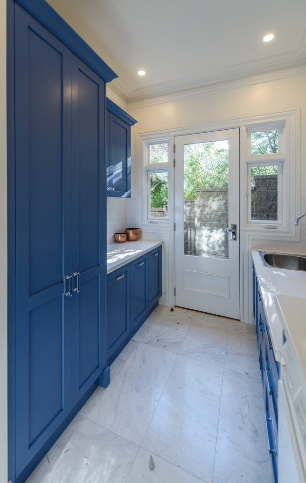 Inspiration för mellanstora klassiska parallella tvättstugor enbart för tvätt, med luckor med infälld panel, blå skåp, bänkskiva i kvarts, vita väggar, marmorgolv, en tvättmaskin och torktumlare bredvid varandra och en nedsänkt diskho