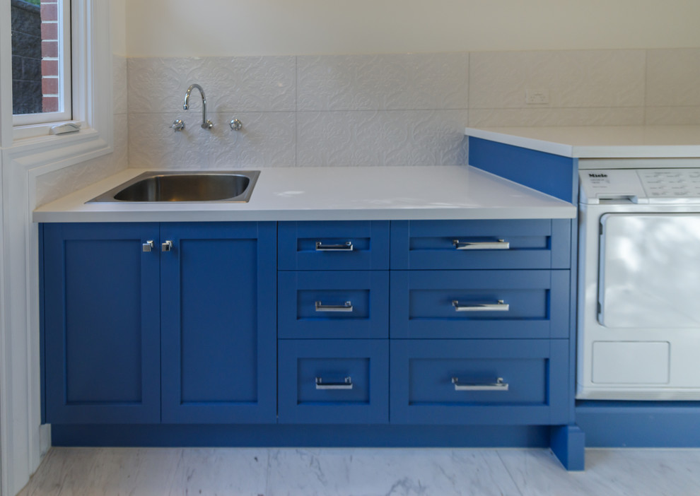 Inspiration för en mellanstor vintage parallell tvättstuga enbart för tvätt, med en enkel diskho, luckor med infälld panel, blå skåp, bänkskiva i kvarts, vita väggar, marmorgolv och en tvättmaskin och torktumlare bredvid varandra