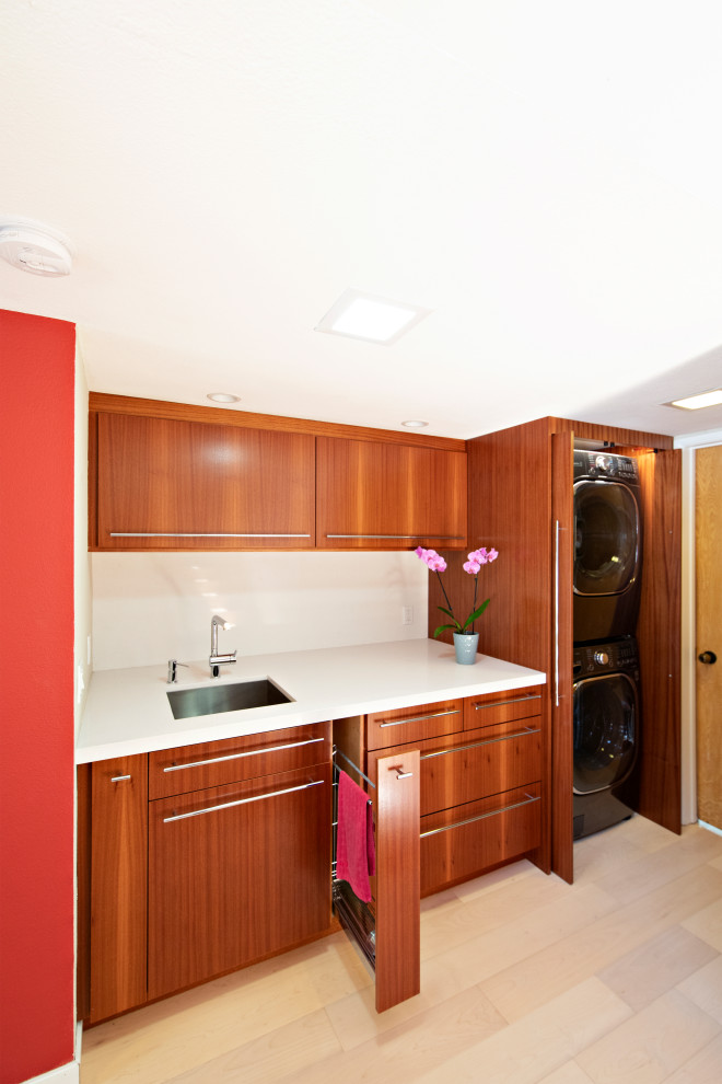 サンディエゴにあるお手頃価格の小さなモダンスタイルのおしゃれな家事室 (I型、アンダーカウンターシンク、フラットパネル扉のキャビネット、中間色木目調キャビネット、クオーツストーンカウンター、赤い壁、淡色無垢フローリング、目隠し付き洗濯機・乾燥機、茶色い床、白いキッチンカウンター) の写真