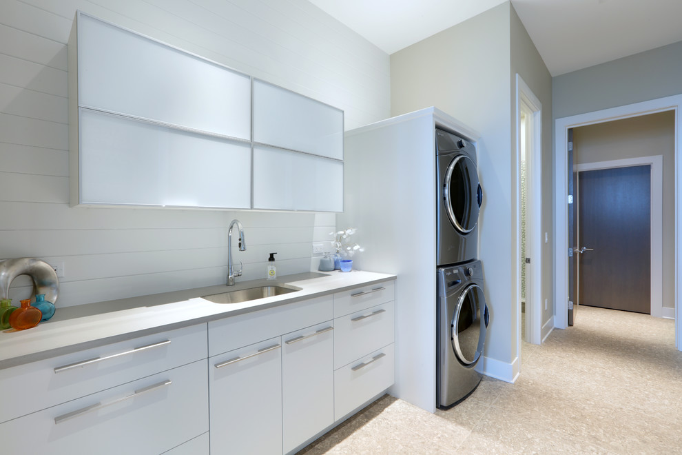Foto på en stor funkis grå parallell tvättstuga enbart för tvätt, med en undermonterad diskho, luckor med glaspanel, vita skåp, bänkskiva i kvarts, grå väggar, klinkergolv i keramik, en tvättpelare och grått golv