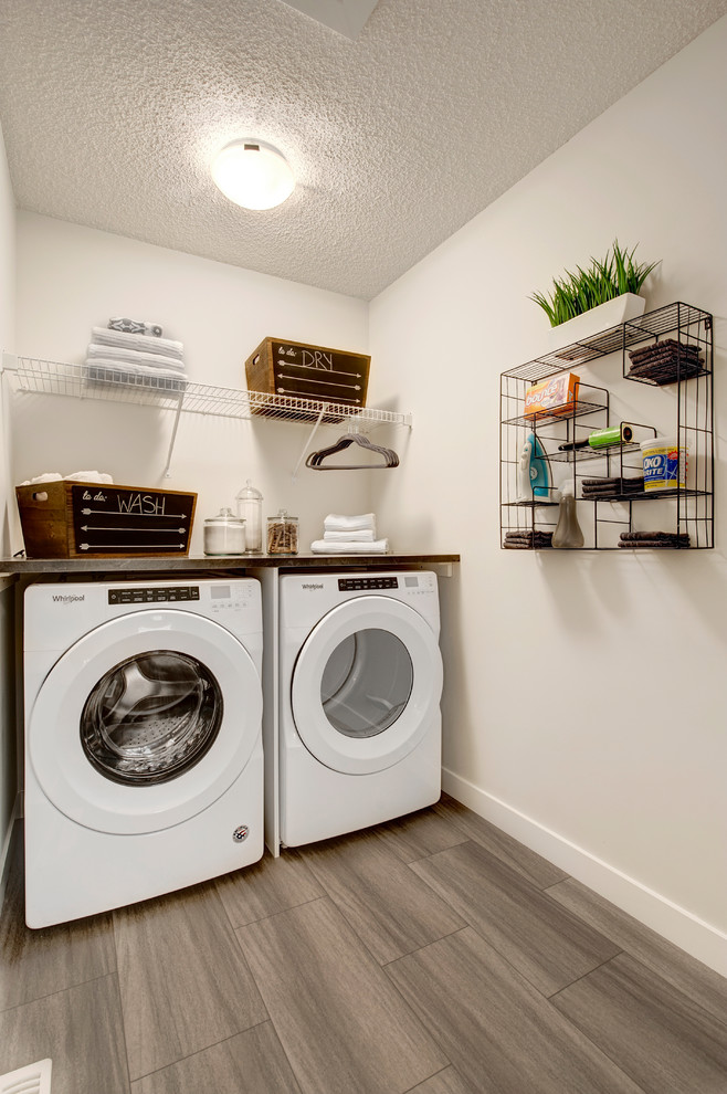 Diseño de cuarto de lavado lineal clásico renovado pequeño con encimera de laminado, paredes blancas, suelo vinílico, lavadora y secadora juntas, suelo gris y encimeras negras