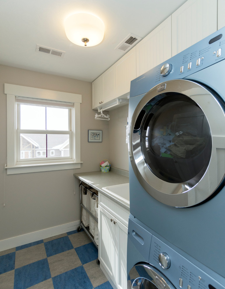 Inspiration for a mid-sized timeless single-wall dedicated laundry room remodel in Other with white cabinets, laminate countertops, gray walls, a stacked washer/dryer and a drop-in sink
