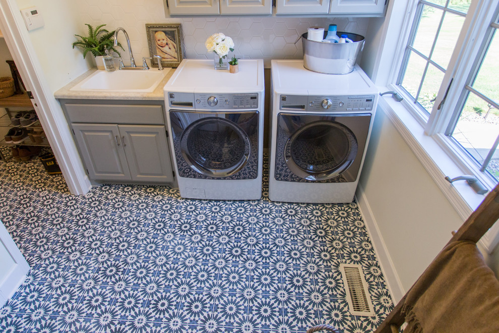 Inredning av en modern stor tvättstuga enbart för tvätt, med betonggolv, en tvättmaskin och torktumlare bredvid varandra, blått golv, en nedsänkt diskho, luckor med upphöjd panel och grå väggar