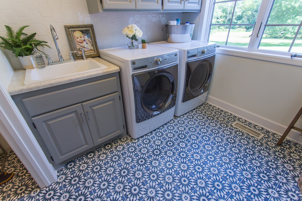 Bild på en stor funkis tvättstuga enbart för tvätt, med betonggolv, en tvättmaskin och torktumlare bredvid varandra, blått golv, en nedsänkt diskho, luckor med upphöjd panel och grå väggar