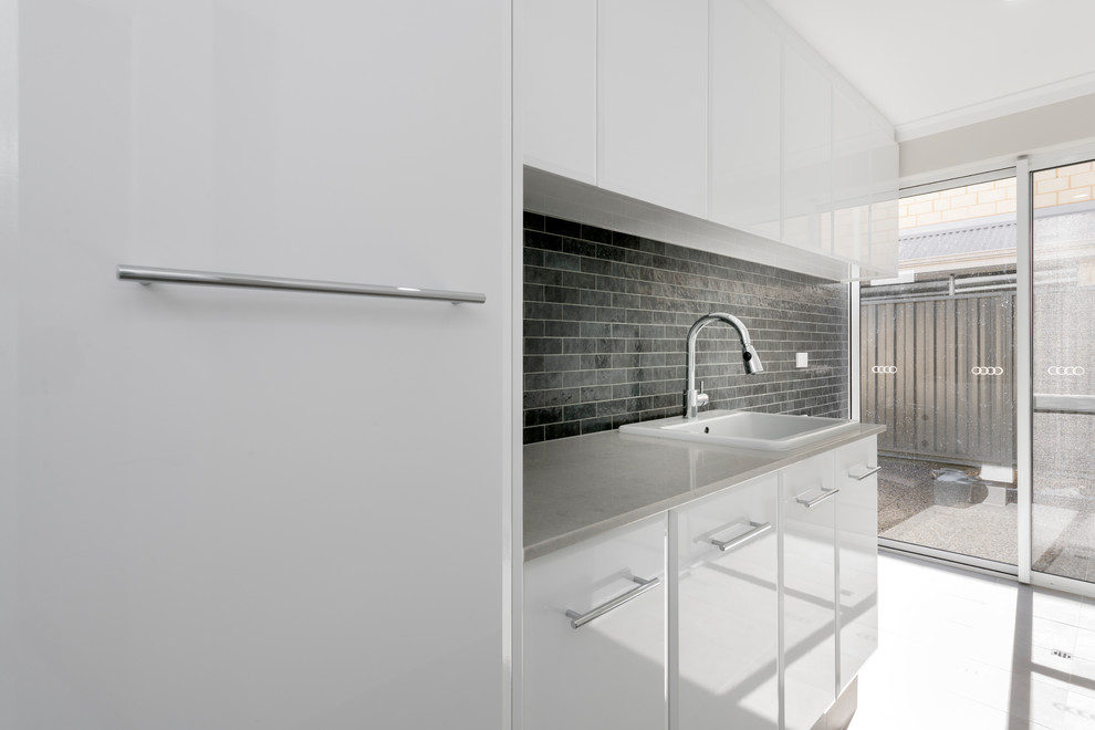 Modern single-wall separated utility room in Perth with a built-in sink, white cabinets, composite countertops, black walls, porcelain flooring, grey floors and grey worktops.