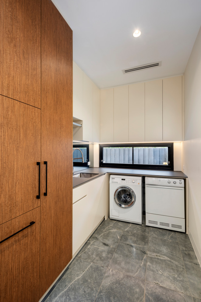 Mittelgroße Moderne Waschküche in L-Form mit Unterbauwaschbecken, flächenbündigen Schrankfronten, hellbraunen Holzschränken, Kalkstein und Waschmaschine und Trockner nebeneinander in Melbourne