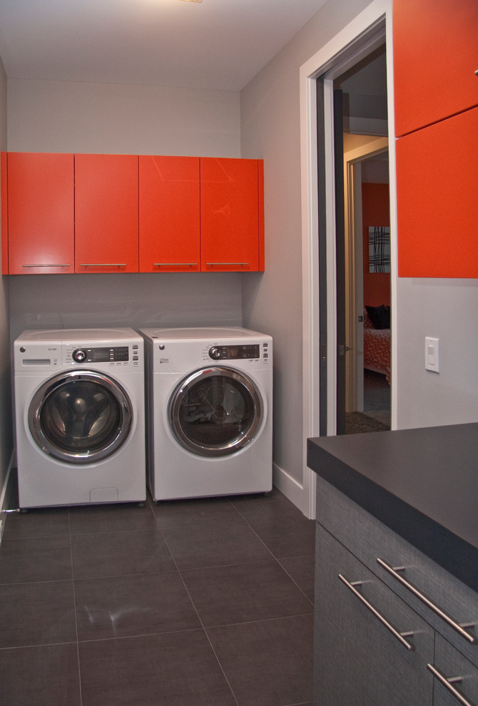 Modelo de lavadero multiusos y lineal actual grande con armarios con paneles lisos, lavadora y secadora juntas y puertas de armario rojas