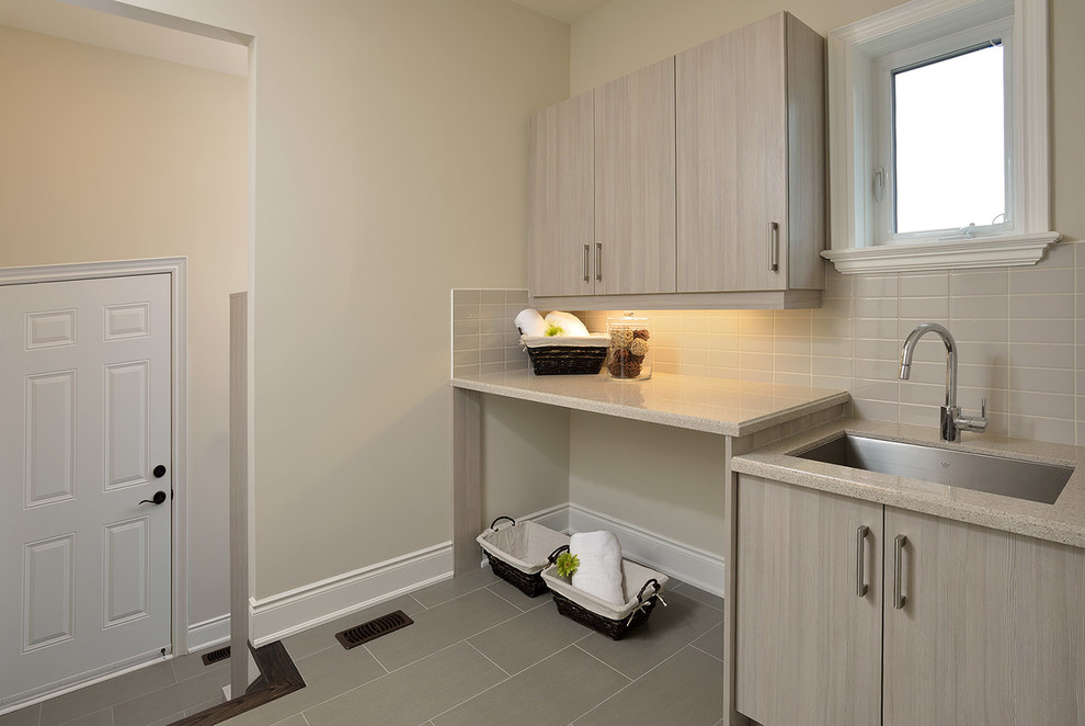Dedicated laundry room - mid-sized transitional single-wall porcelain tile and gray floor dedicated laundry room idea in Toronto with a single-bowl sink, flat-panel cabinets, light wood cabinets, beige walls and beige countertops