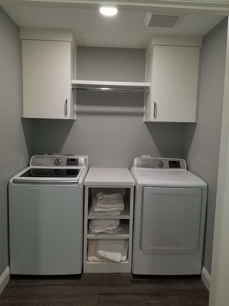 Photo of a small classic single-wall separated utility room in Dallas with flat-panel cabinets, white cabinets, laminate countertops, grey walls, laminate floors, a side by side washer and dryer, brown floors and white worktops.